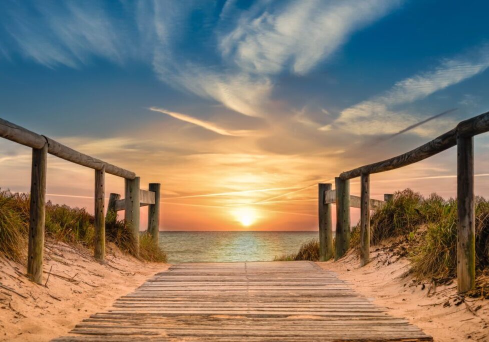 Sunset over beach with wooden pathway.