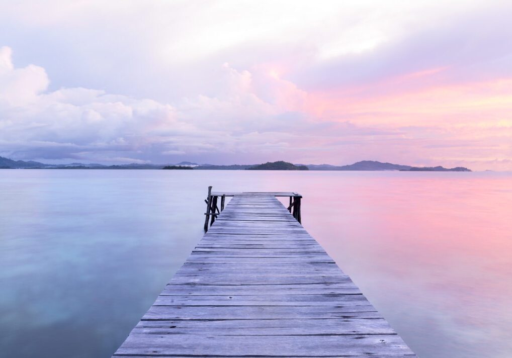 Wooden pier over calm, pastel-colored sea.
